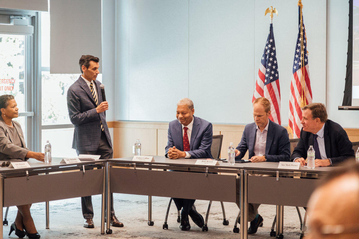 One man standing in between four people sitting at a table 