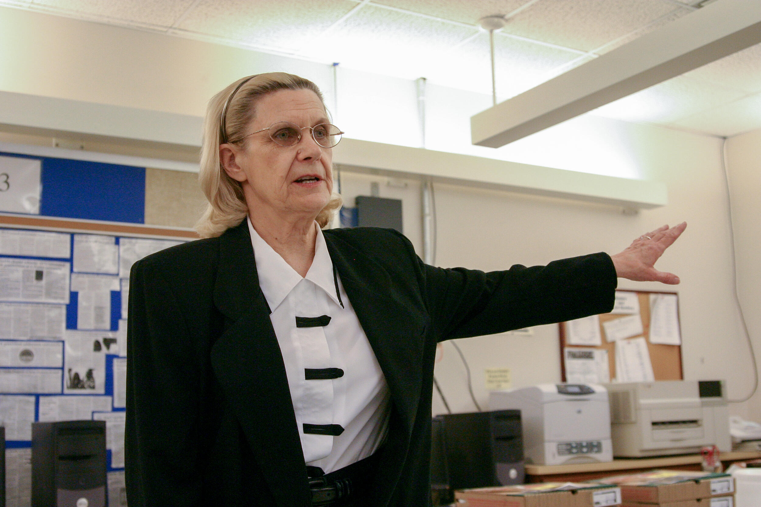 A photo of a woman from the waist up. She has her right arm outstretched to the right of her. 