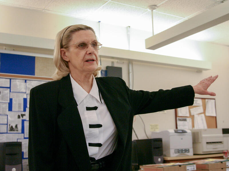 A photo of a woman from the waist up. She has her right arm outstretched to the right of her. 