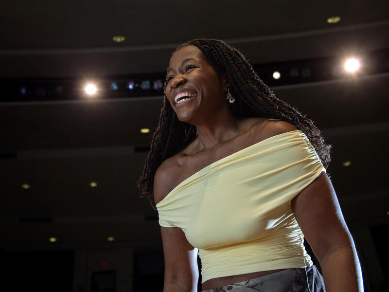 A photo of a woman from the chest up. She is smiling and wearing a yellow, off the shoulders shirt. 