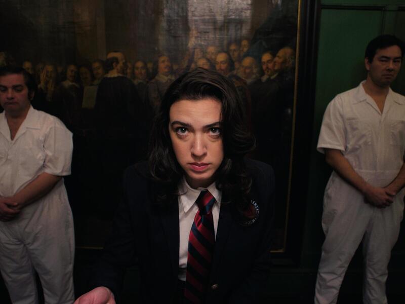 A photo of a woman in a suit and tie standing in between two people wearing all white outfits. 