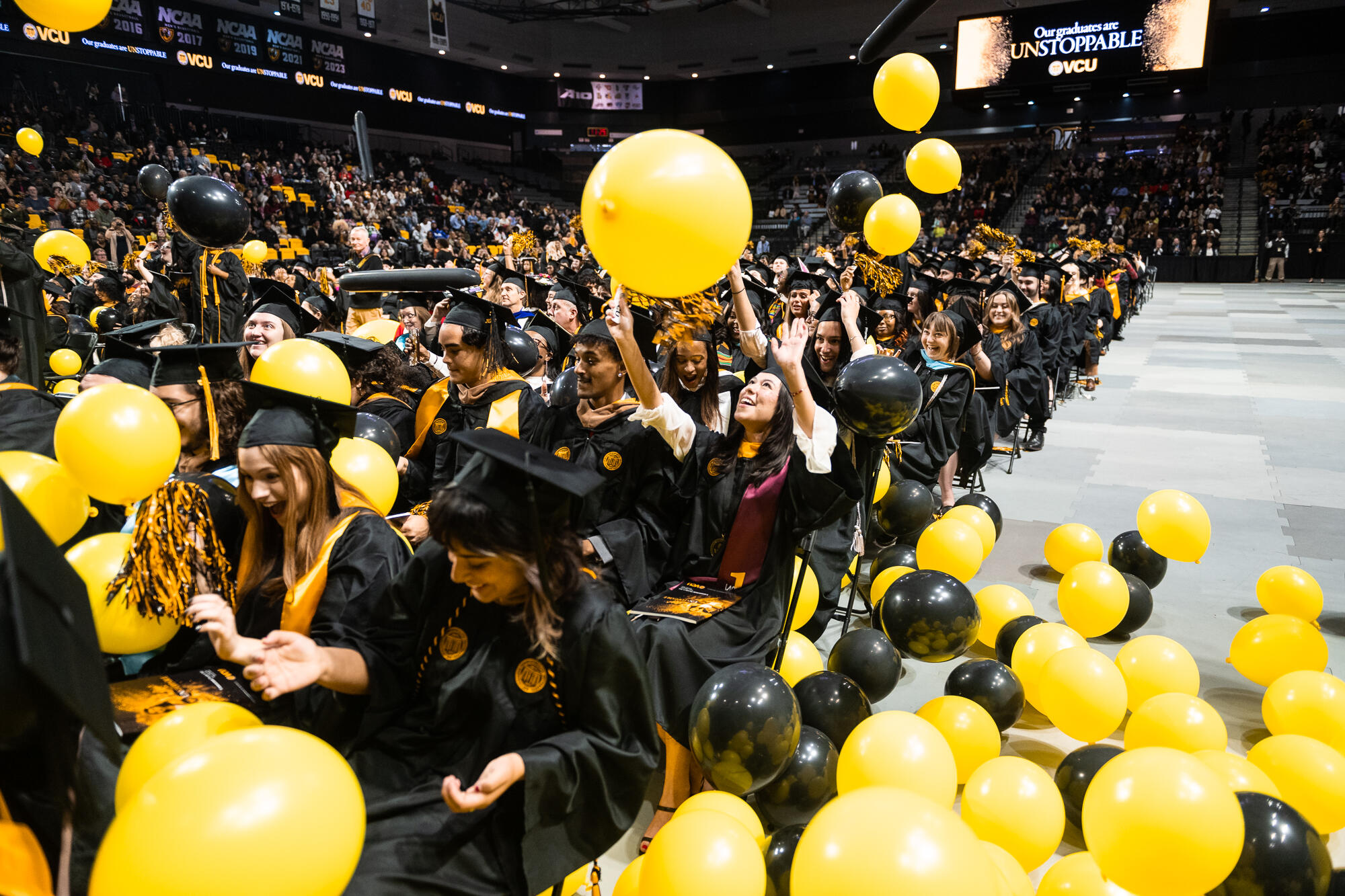 A photo of a crowd of students sitting in chairs with yellow and black baloons raining down on them