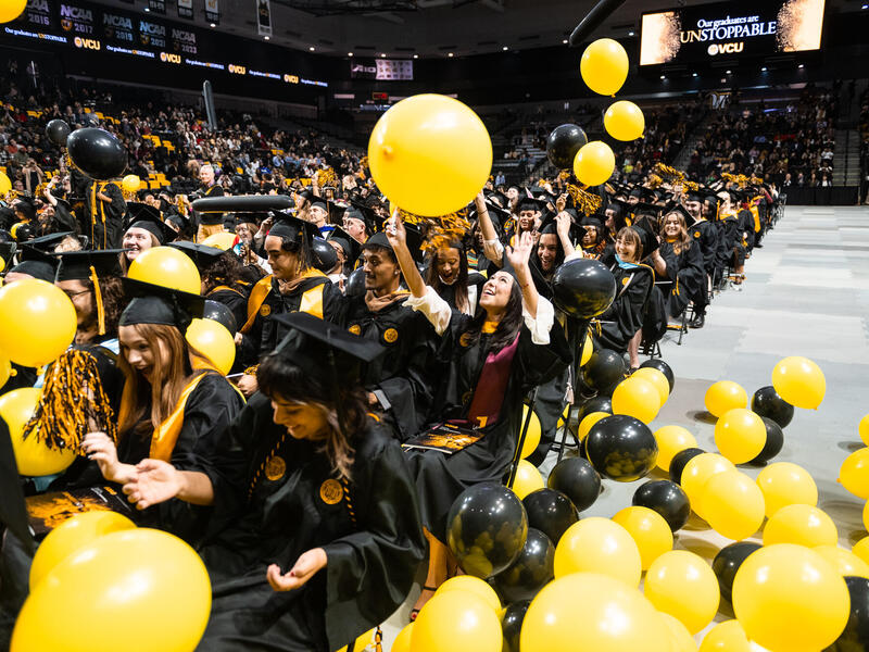 A photo of a crowd of students sitting in chairs with yellow and black baloons raining down on them