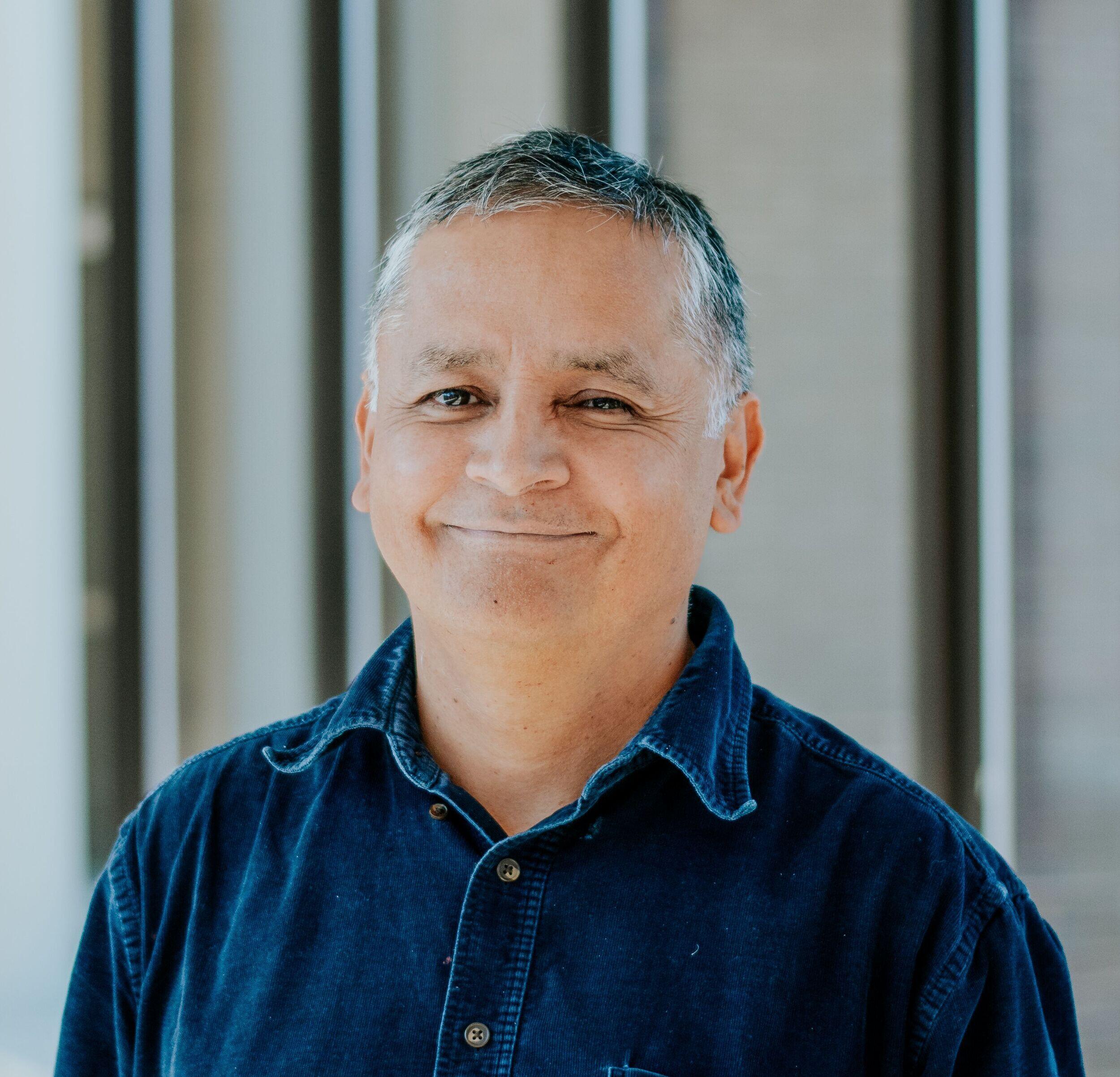 Head and shoulders image of a man in a blue collared shirt.