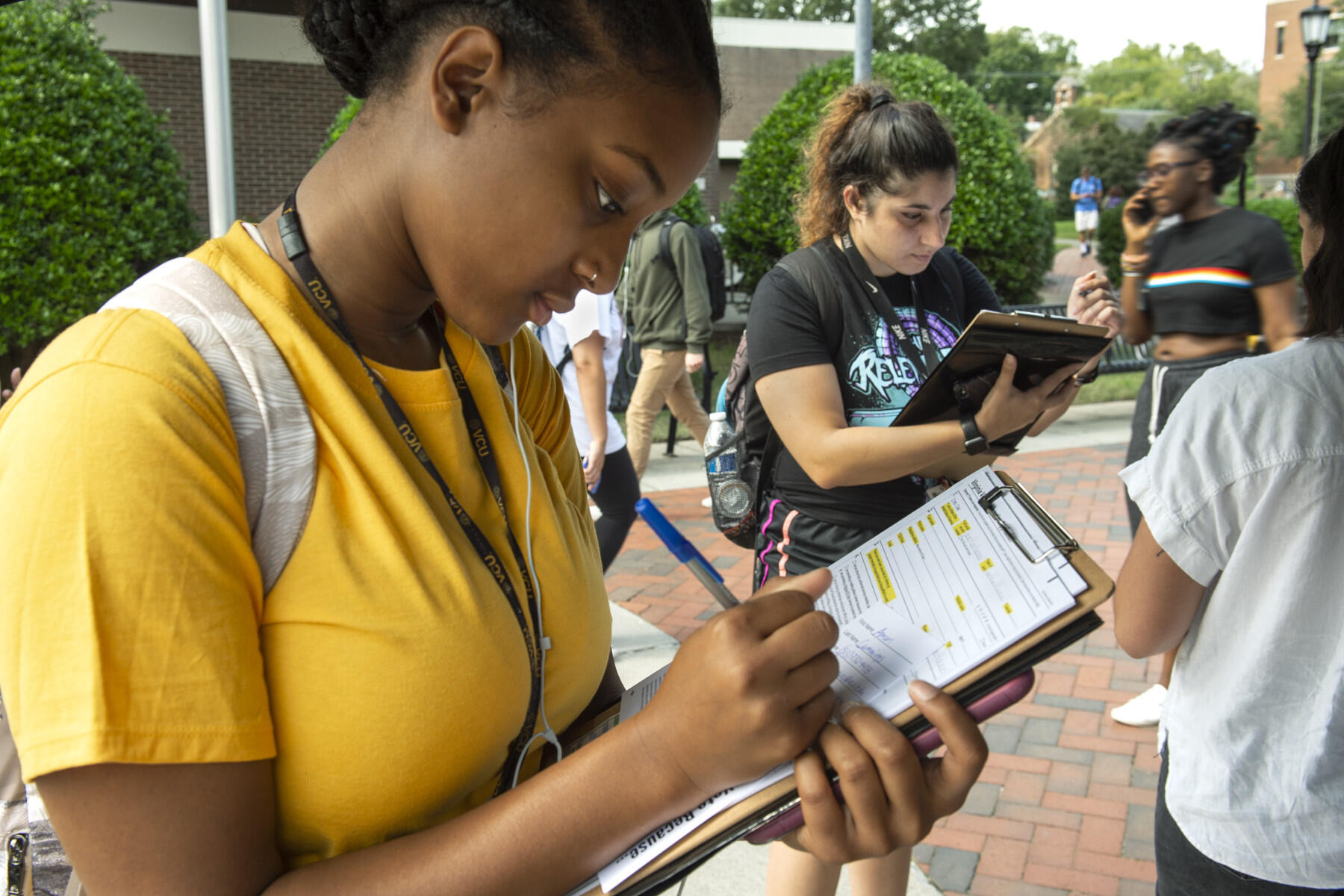 A woman in a yellow T-shirt signs a paper on a clipboard.