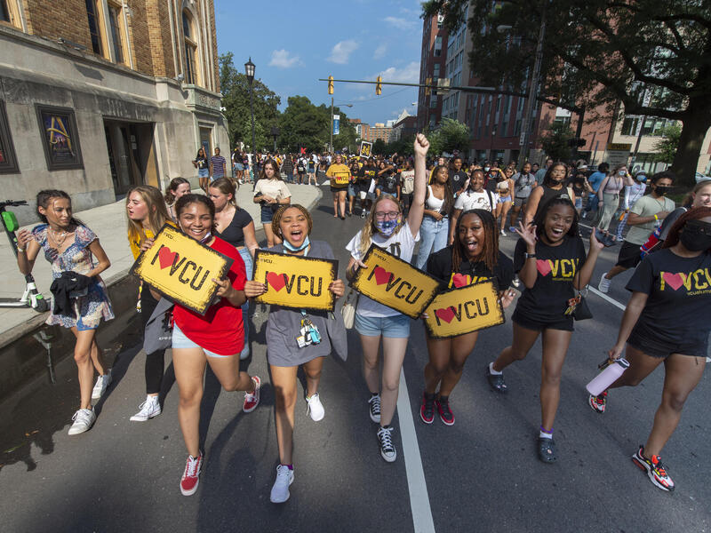 Students walking down the street holding signs that say \"I heart VCU.\"