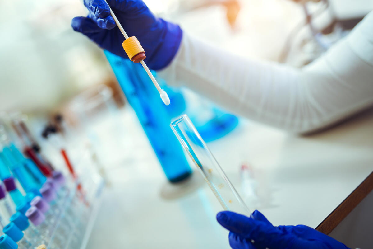 A person in a laboratory holding a swab and a glass tube.