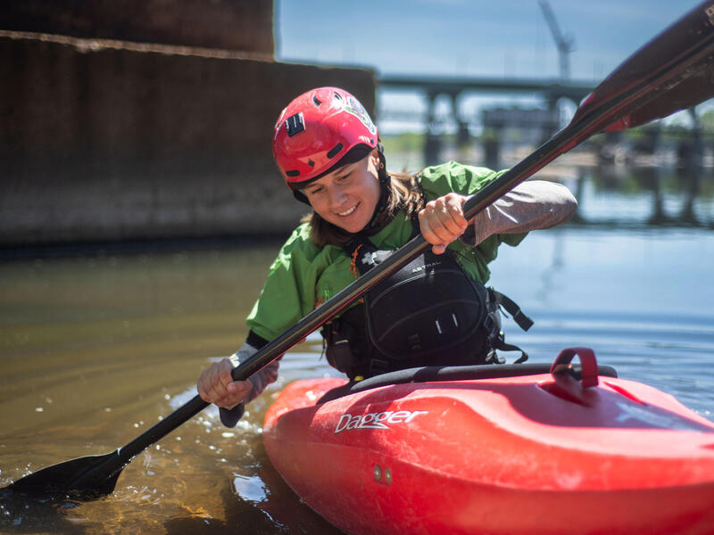 A photo of a woman paddling on a kyak in a river. 