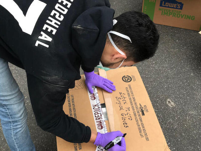A student volunteer packs a box with masks and protective gear to donate to a local hospital.