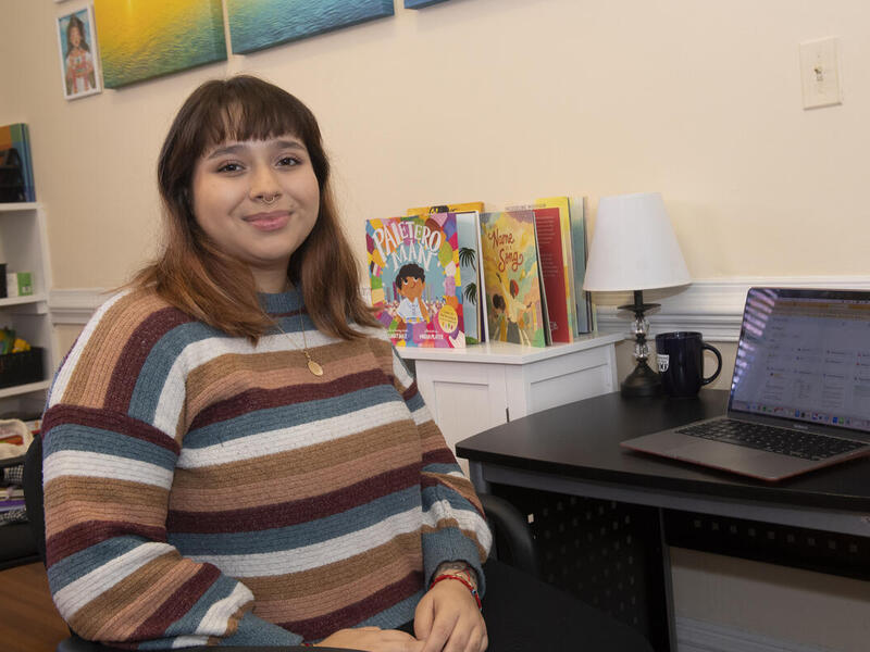 A photo of a woman sitting at a desk with a laptop on it. 