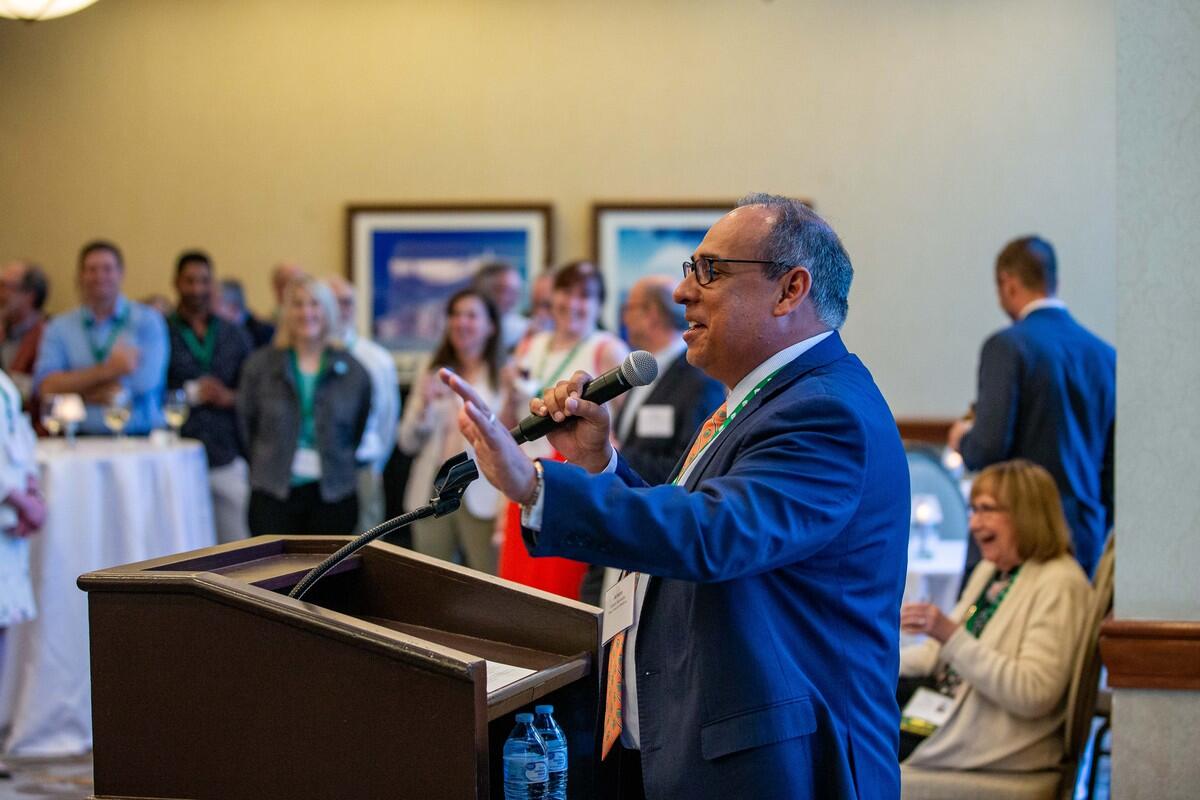 A man speaking at a podium in a room of people 
