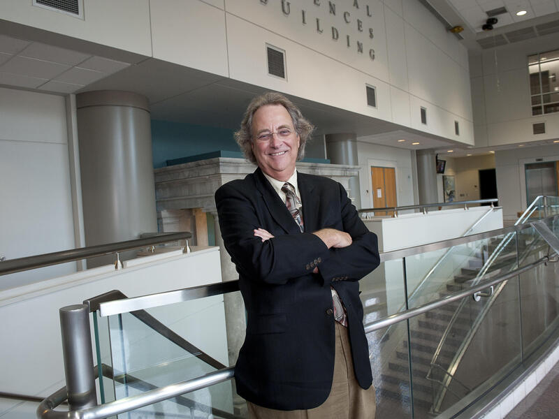 A photo of a man from the waist up. He is standing and smiling with his arms crossed against his chest. 