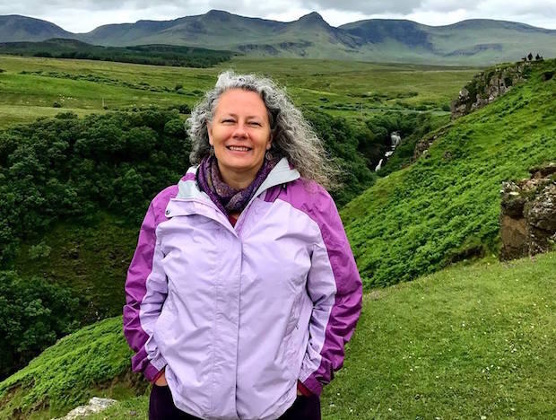 Woman in purple coat standing in green landscape.