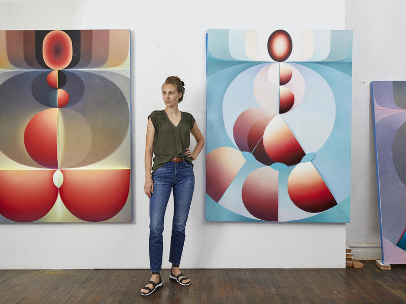 A photo of a woman standing in between two geometric paintings. 