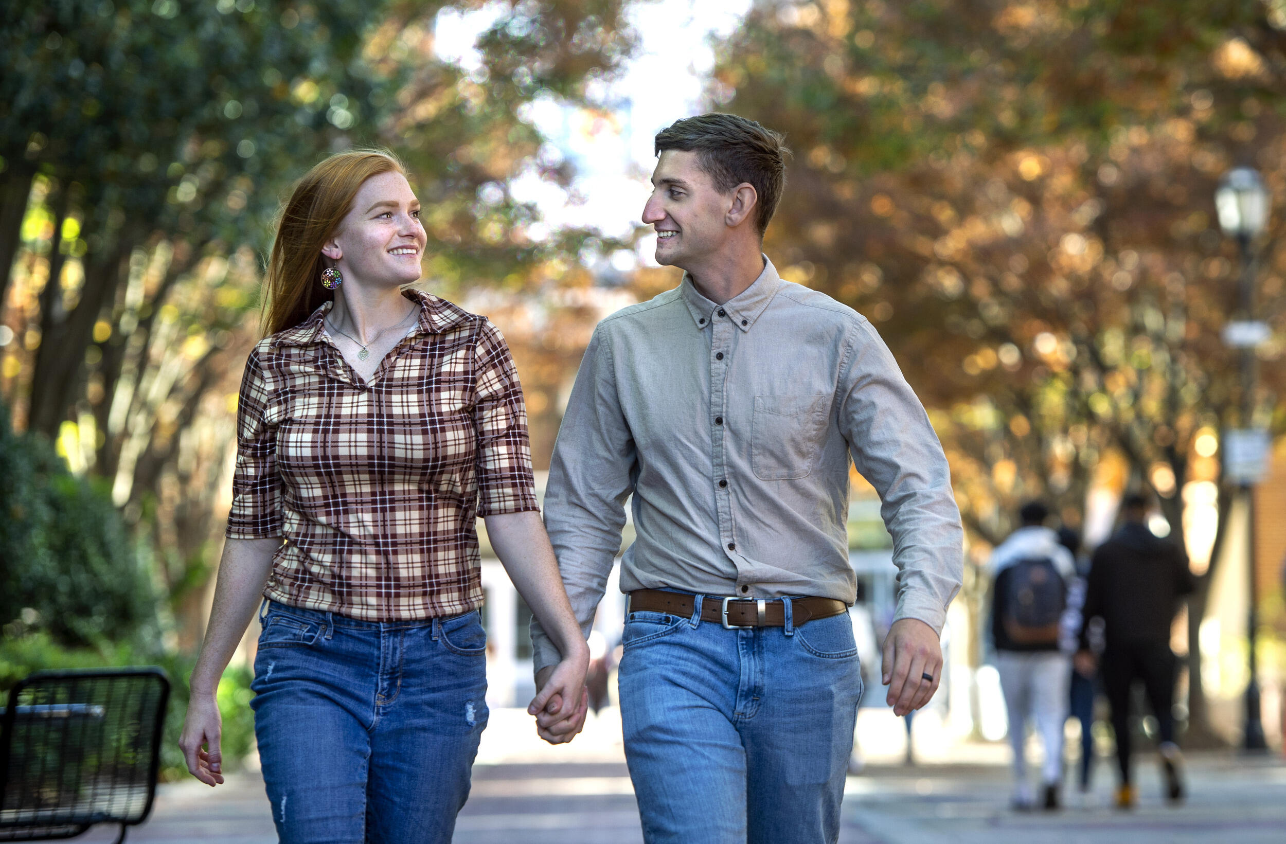 A man and woman walking together while holding hands and looking at each other. 