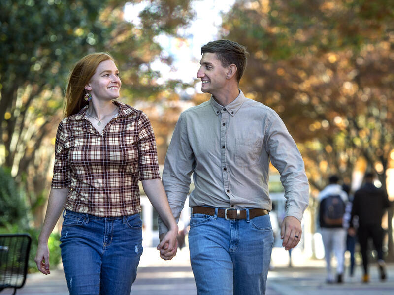 A man and woman walking together while holding hands and looking at each other. 