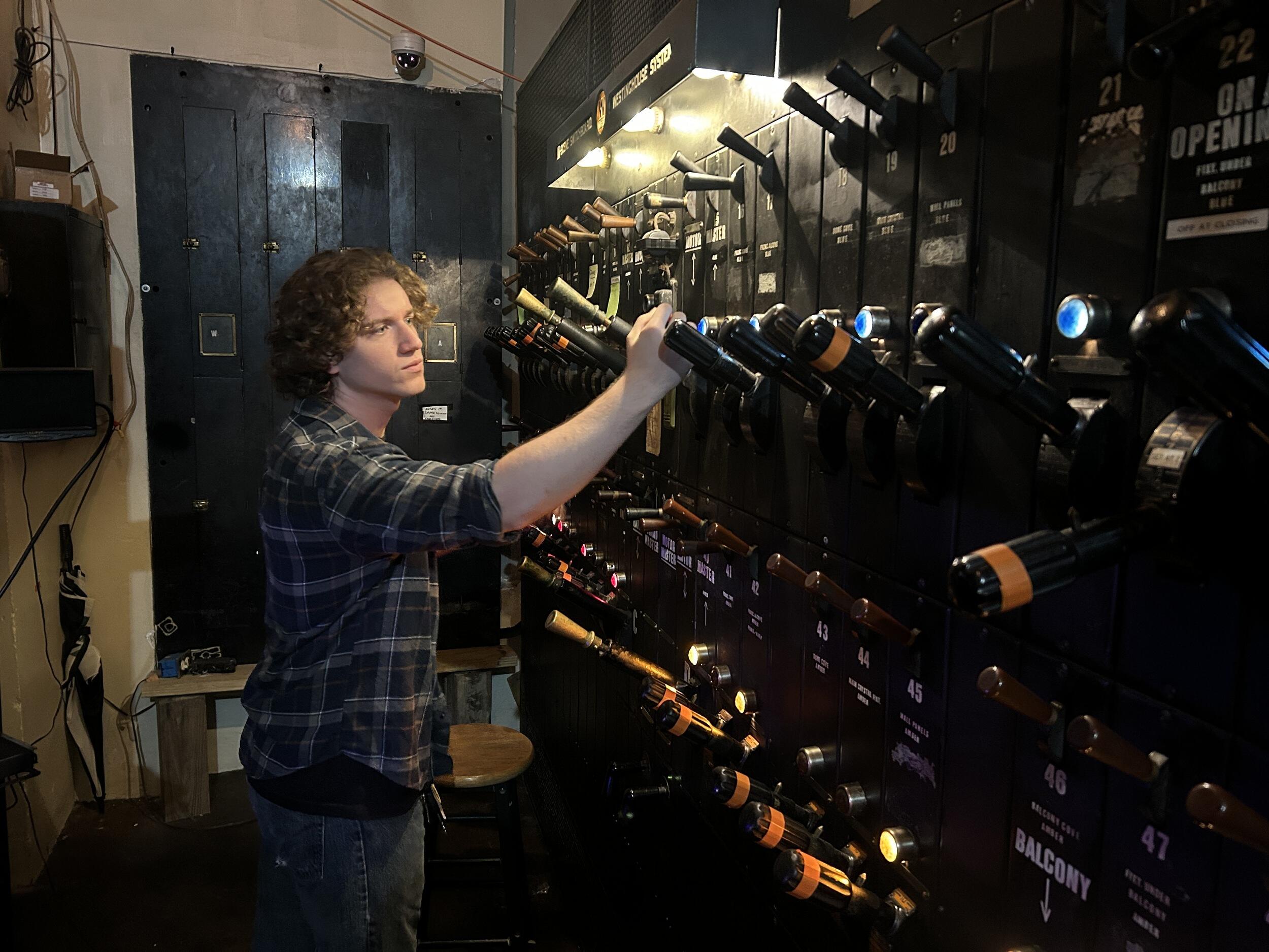 A photo of a man standing next to a large panel of light switches. 