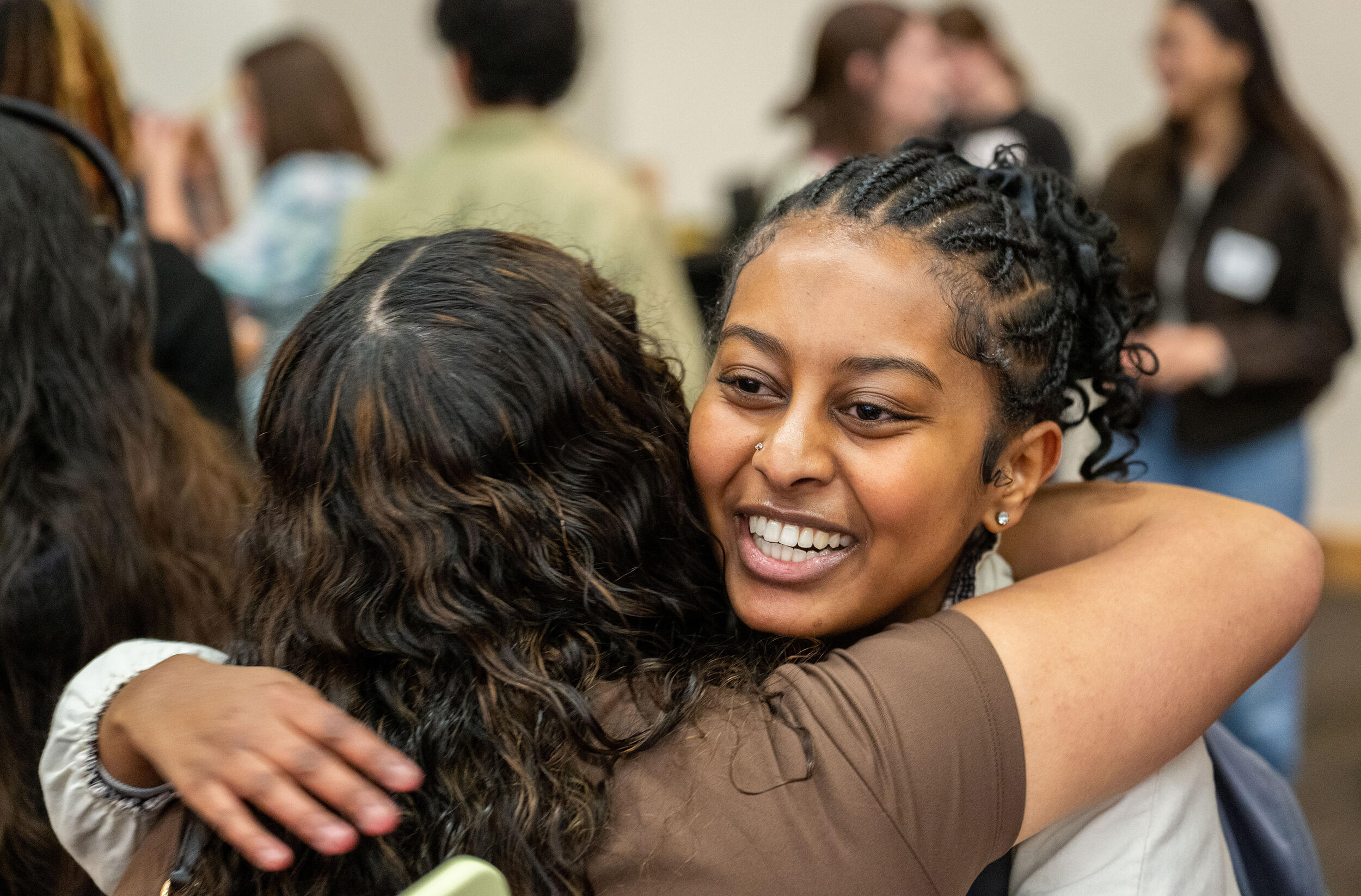 A photo of two women hugging in a room full of people. 