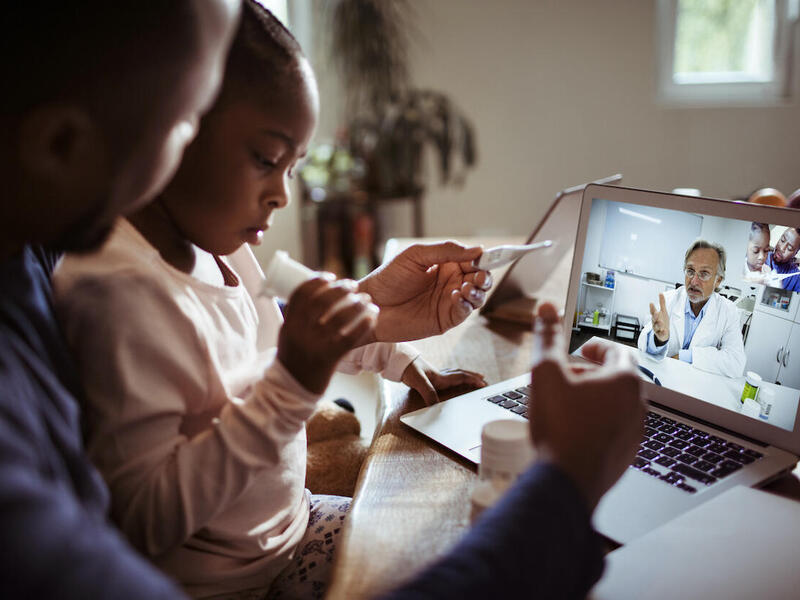 A parent and child participate in a teleconference session with a teacher.