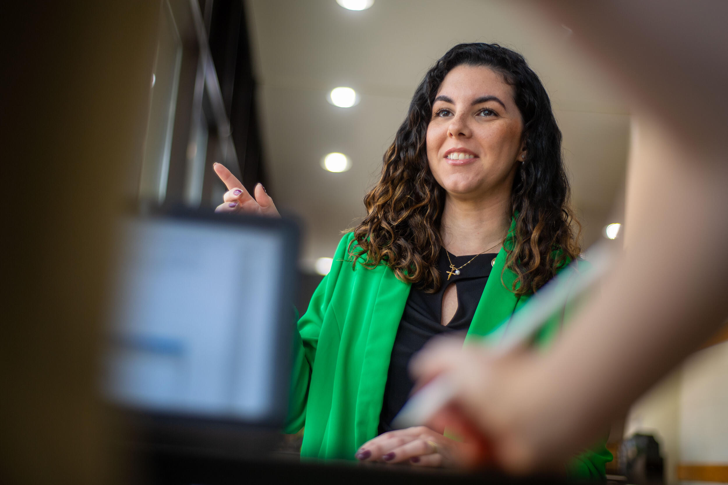 A photo of a woman speaking to a person standing behind a desk. 