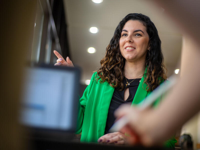 A photo of a woman speaking to a person standing behind a desk. 