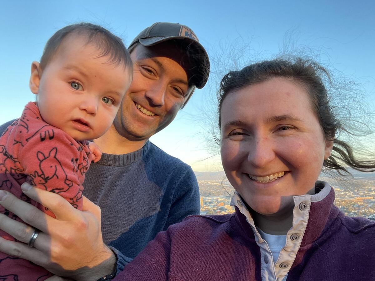 A couple smile at the camera, along with an infant child.