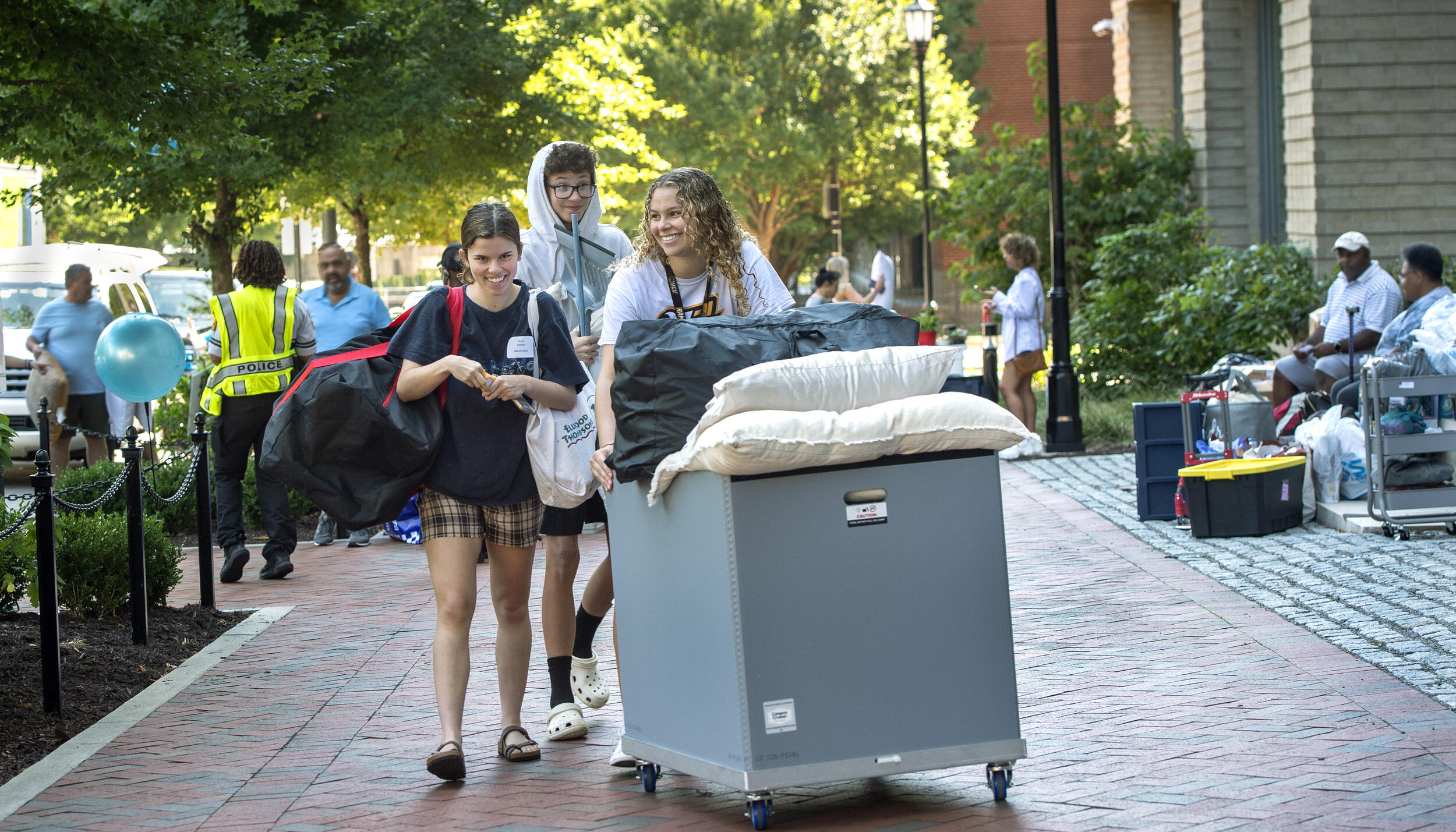 A photo of three students walking with a bin on wheels. 