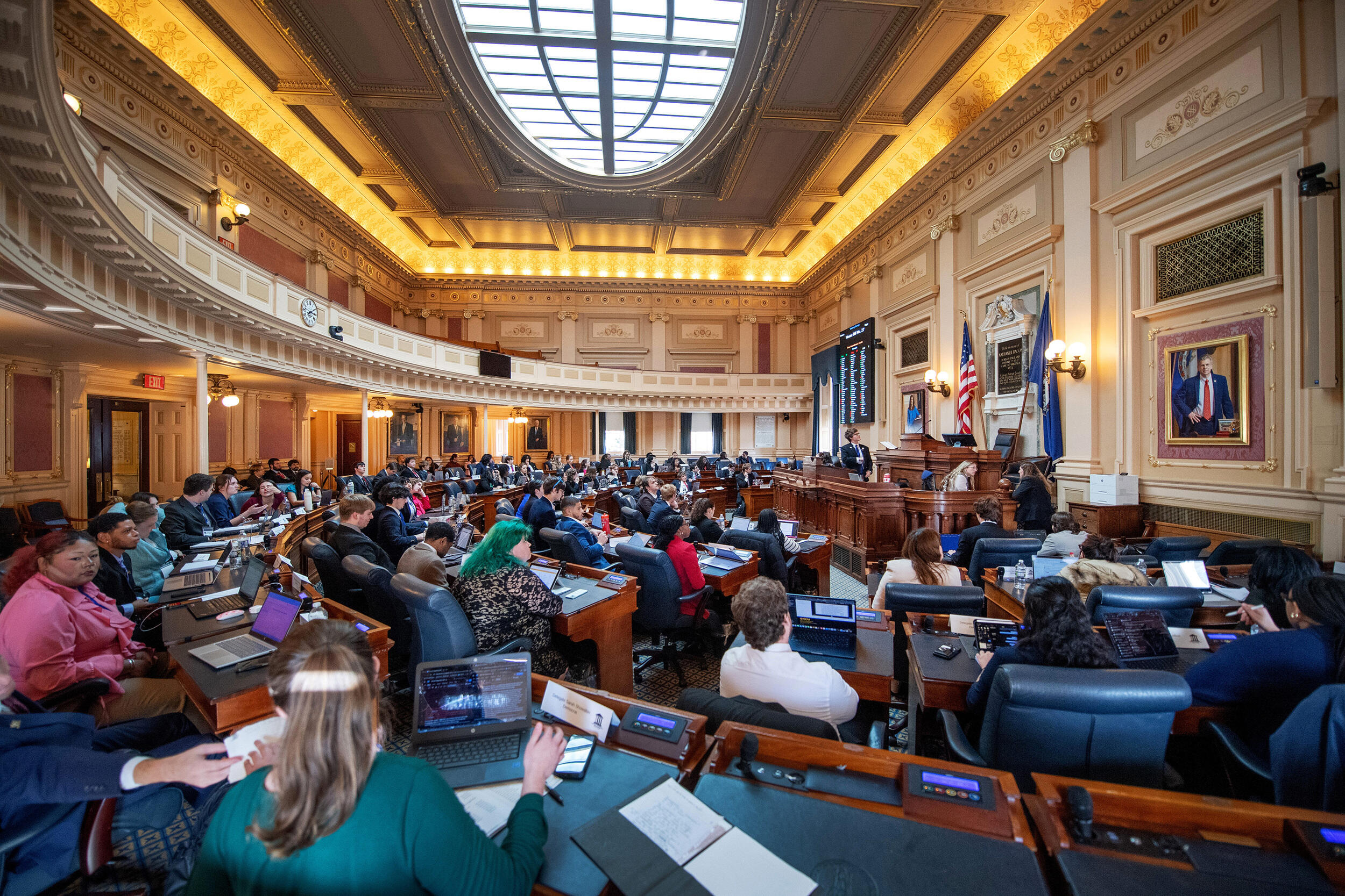 A photo of the floor of the Virginia House of Delegates Chamber filled with college students sitting at the desks. 
