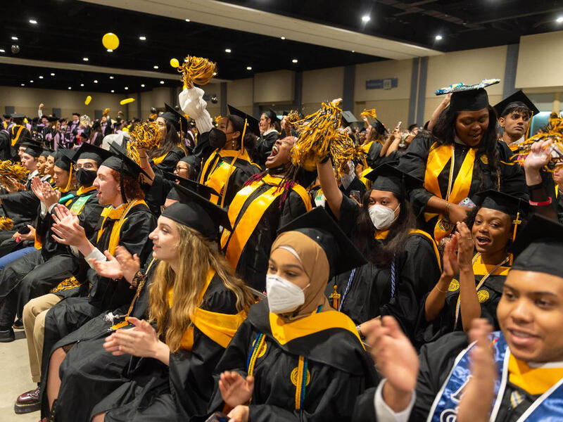 A group of students in graduation regalia sitting and clapping 