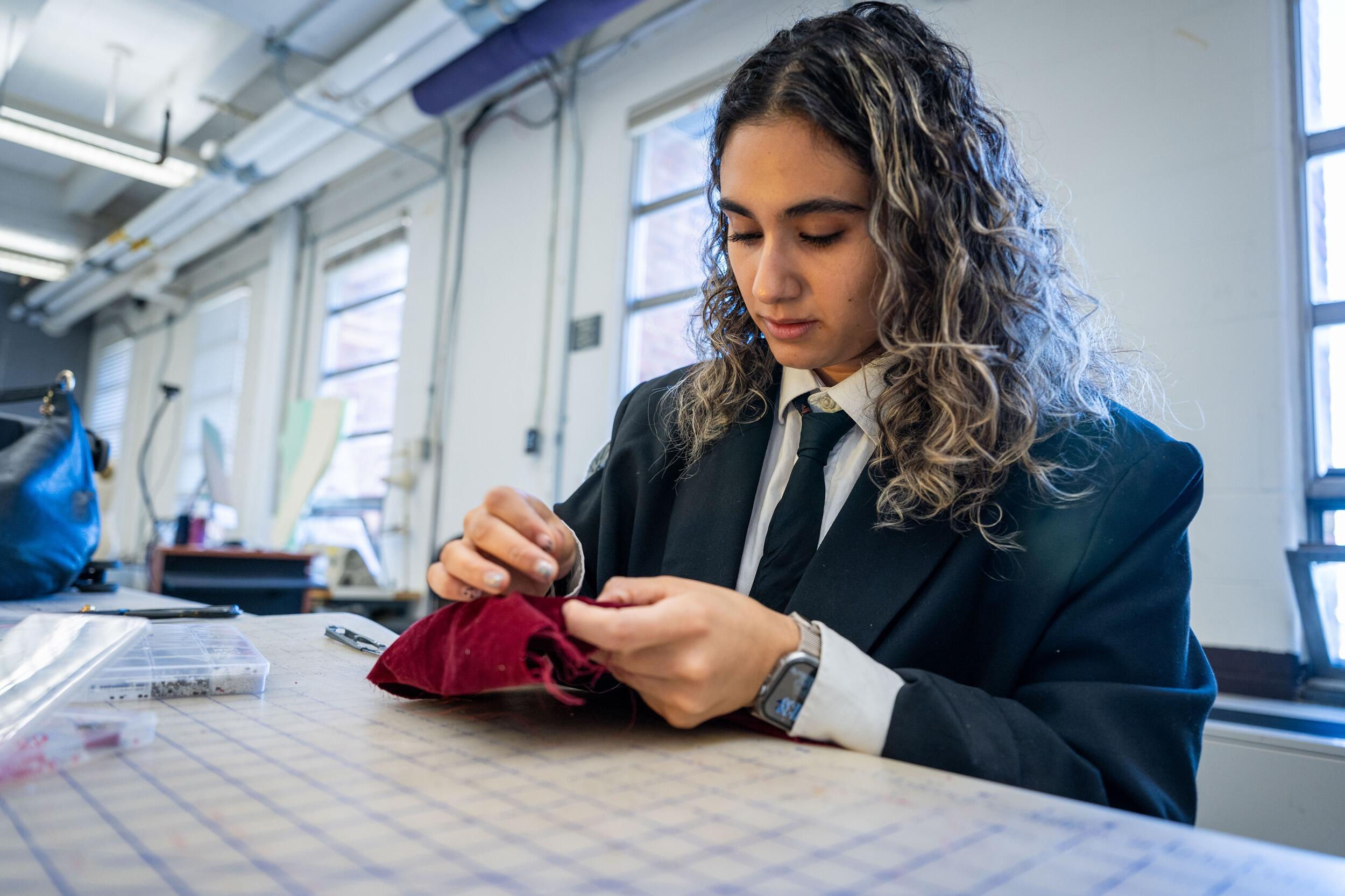 A photo of a woman sitting at a table and sewing. 