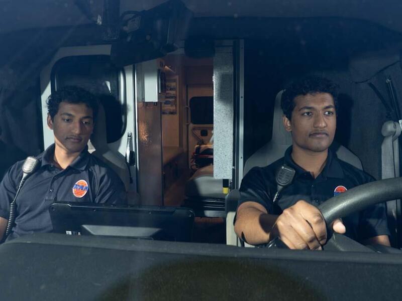 A photo of two men sitting in the front of an ambulance 