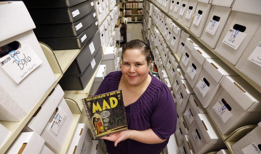 Cindy Jackson holds a rare Mad magazine issue between two rows of shelves of boxes.