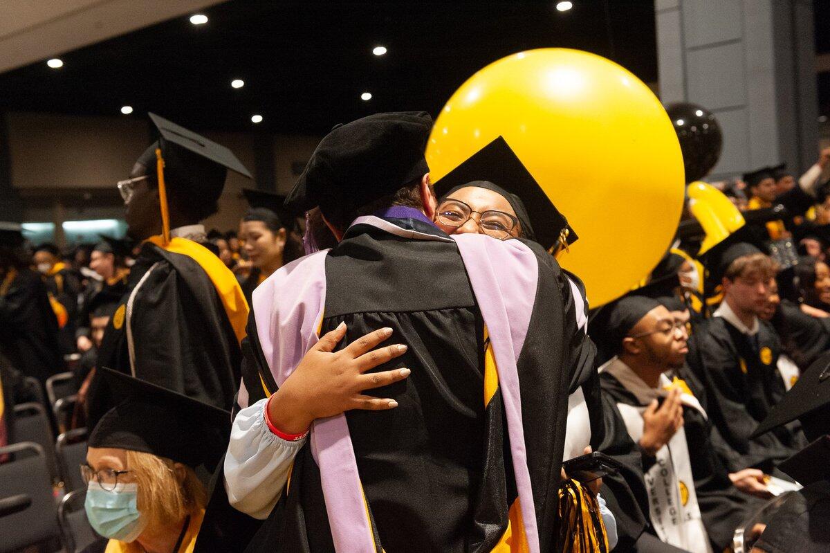 Two students wearing cap and gowns hugging