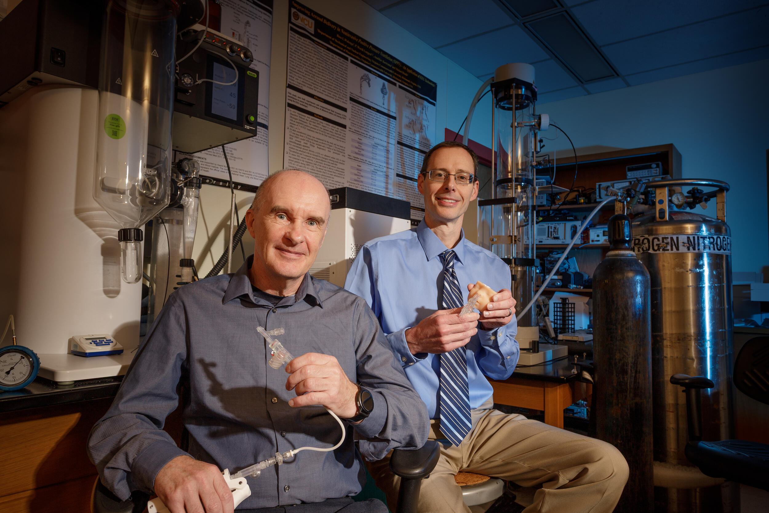 A photo of two men sitting in a labratory. 