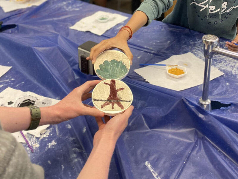 Two teenagers holding two tile circles that look like a tree when next to each other. 