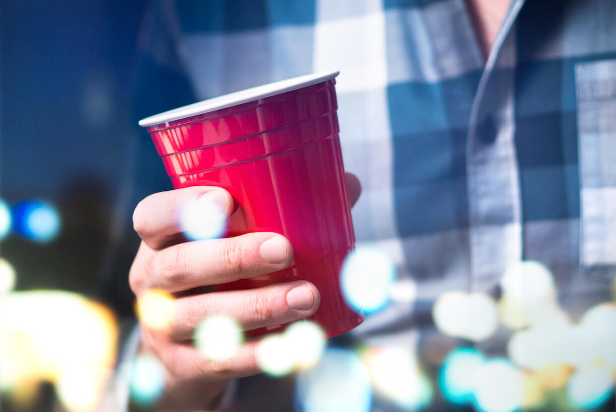 A red plastic cup being held by an individual. Abstract dots of light appear in the foreground.