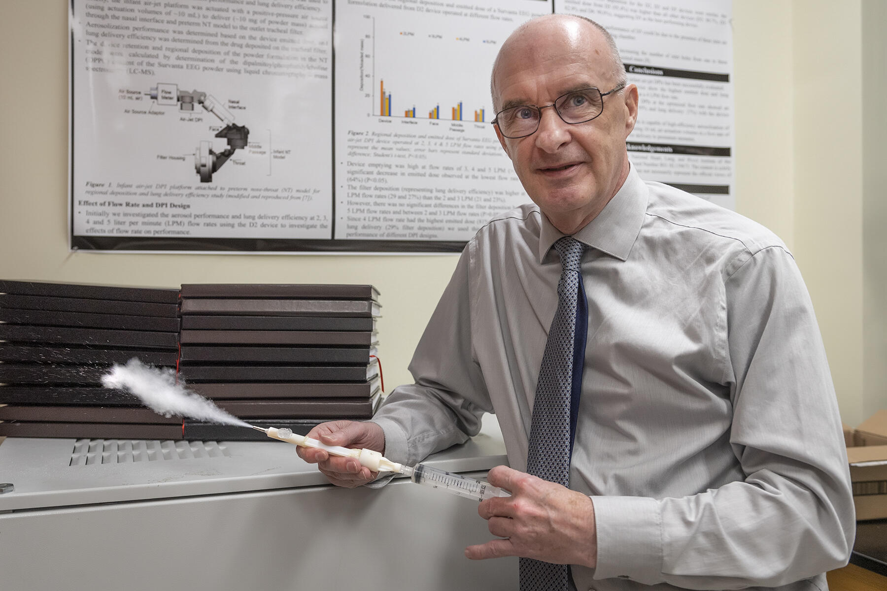 A bald man wearing a light gray button down shirt, darker gray tie, and glasses looking to the right. 