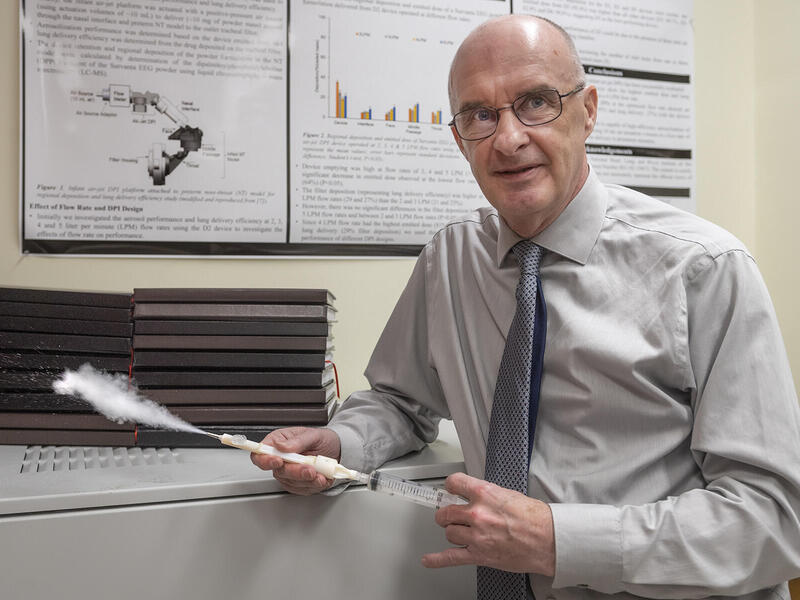 A bald man wearing a light gray button down shirt, darker gray tie, and glasses looking to the right. 