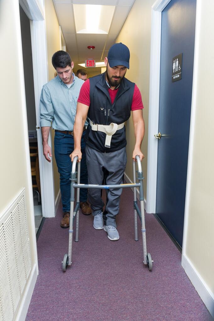Delano provides assistance as a patient practices walking down a hallway in the clinic.