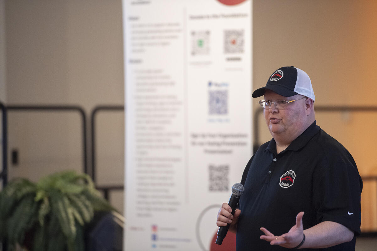 A photo of a man speaking and holding a microphone. 