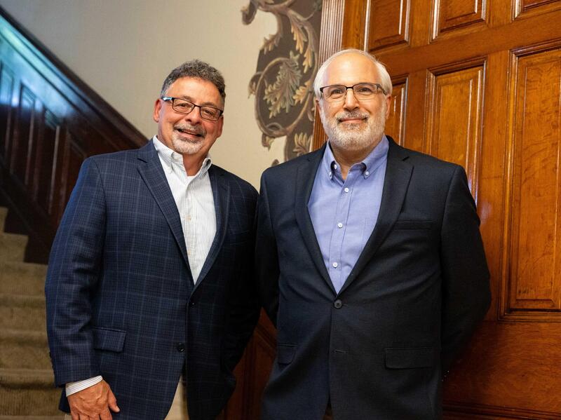 A photo of two men standing by a staircase. 