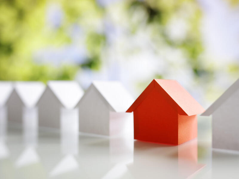 Six model houses sitting on a white surface. The second house to the right is red and all of the other houses are white. 