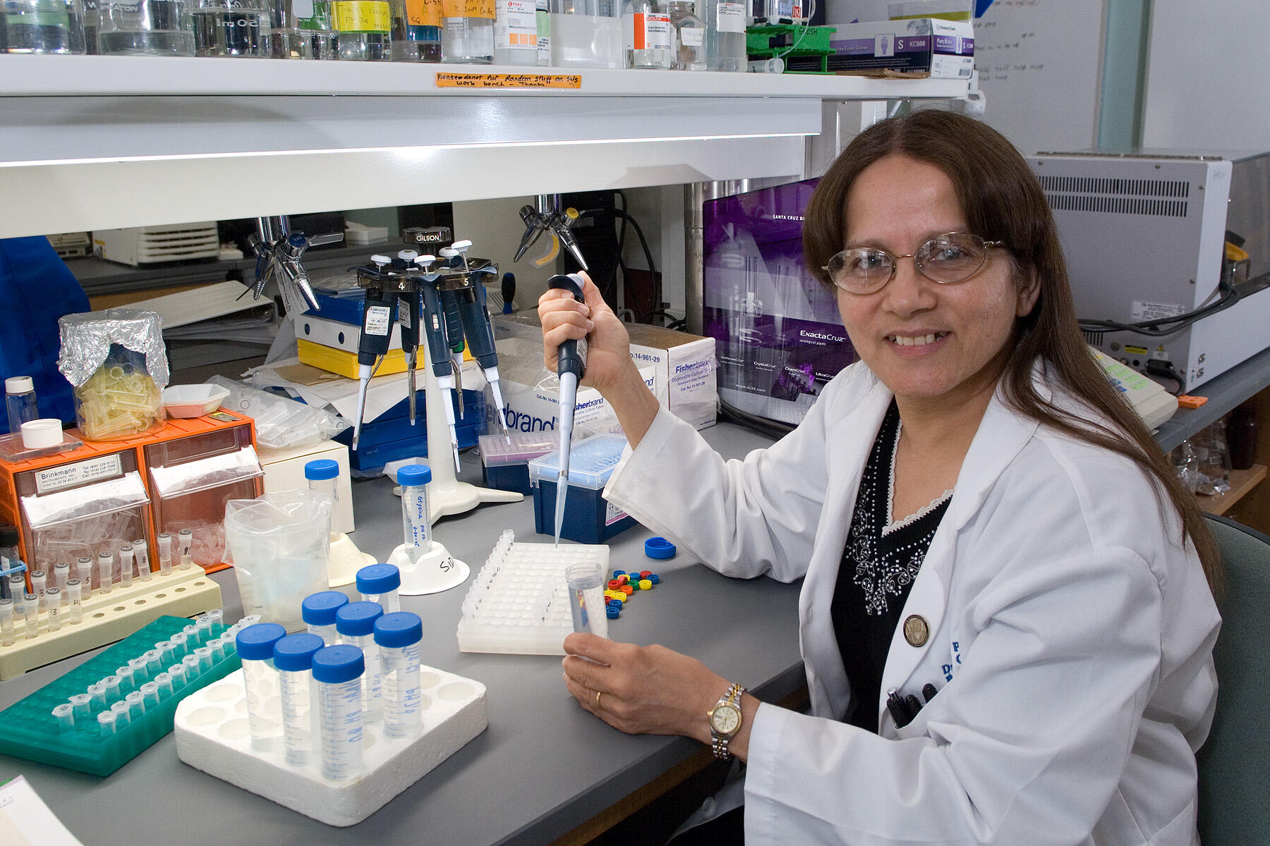 Shobha Gosh sitting at a desk holding a syringe.