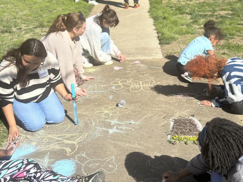 Young adults and children draw images on the sidewalk with chalk.