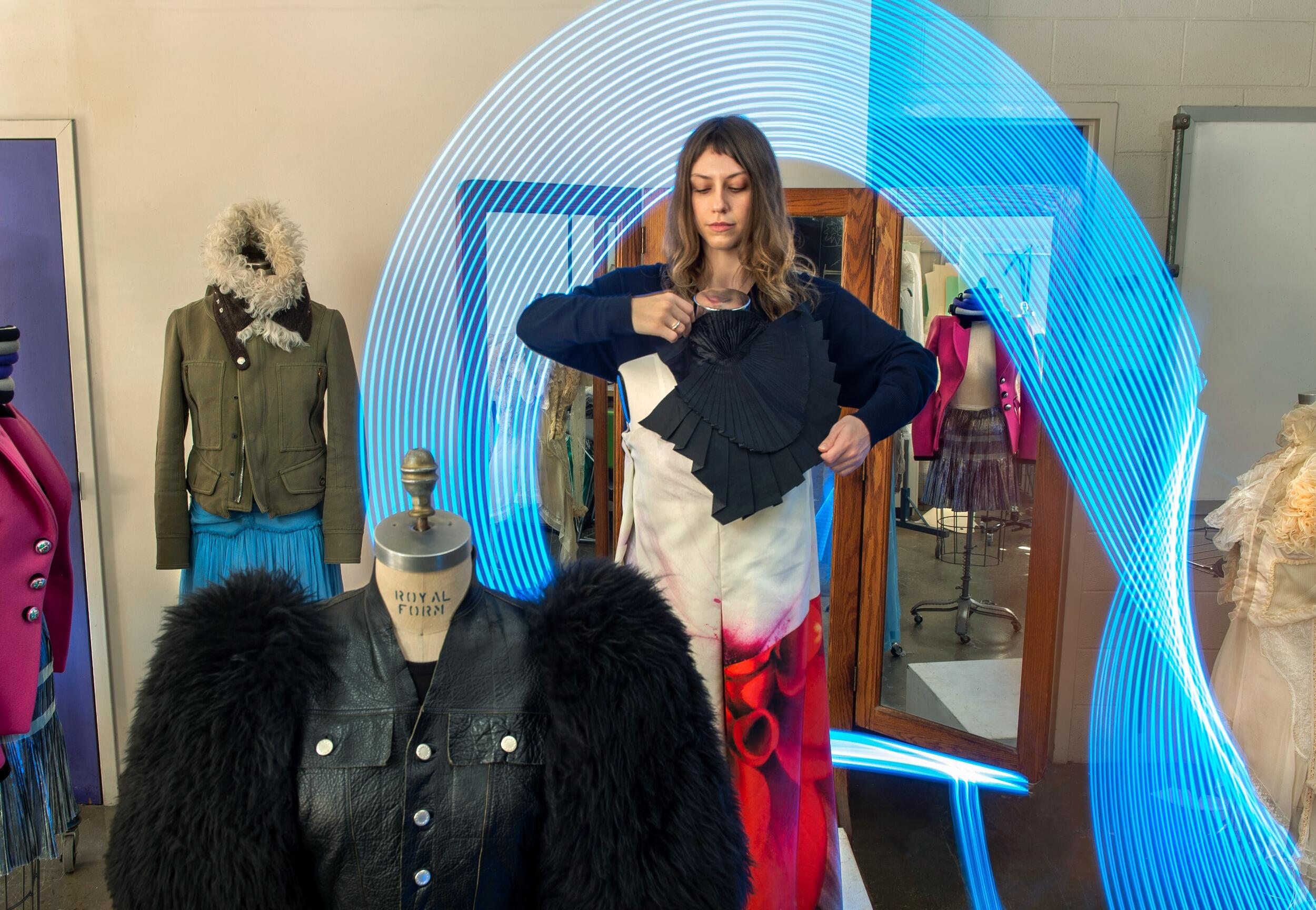 A photo of a woman dressing a maniquin with other maniquins in outfits around her