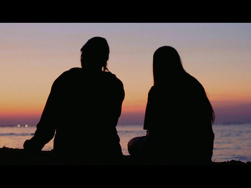 A photo of two people sitting in front of a beach during the sunset. 