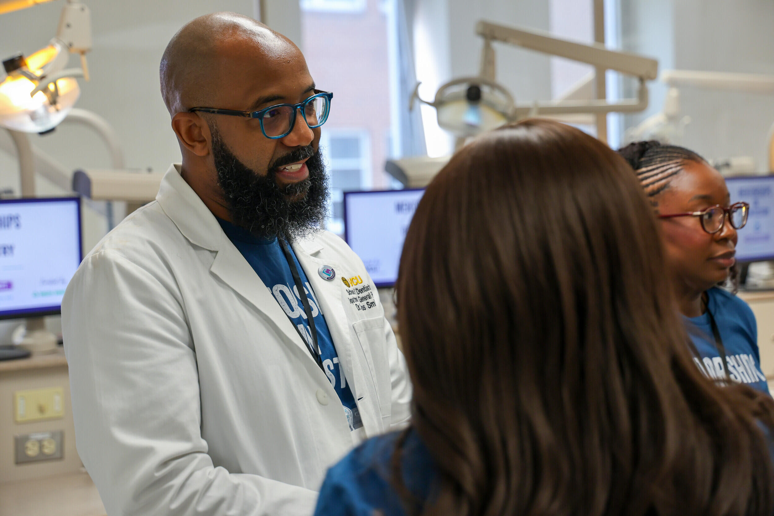 A photo of a man in a white lab coat speaking with two teenage girls in a dental exam room. 