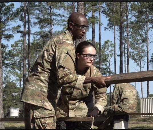 A man and a woman wearing military uniforms and holding planks of wood 