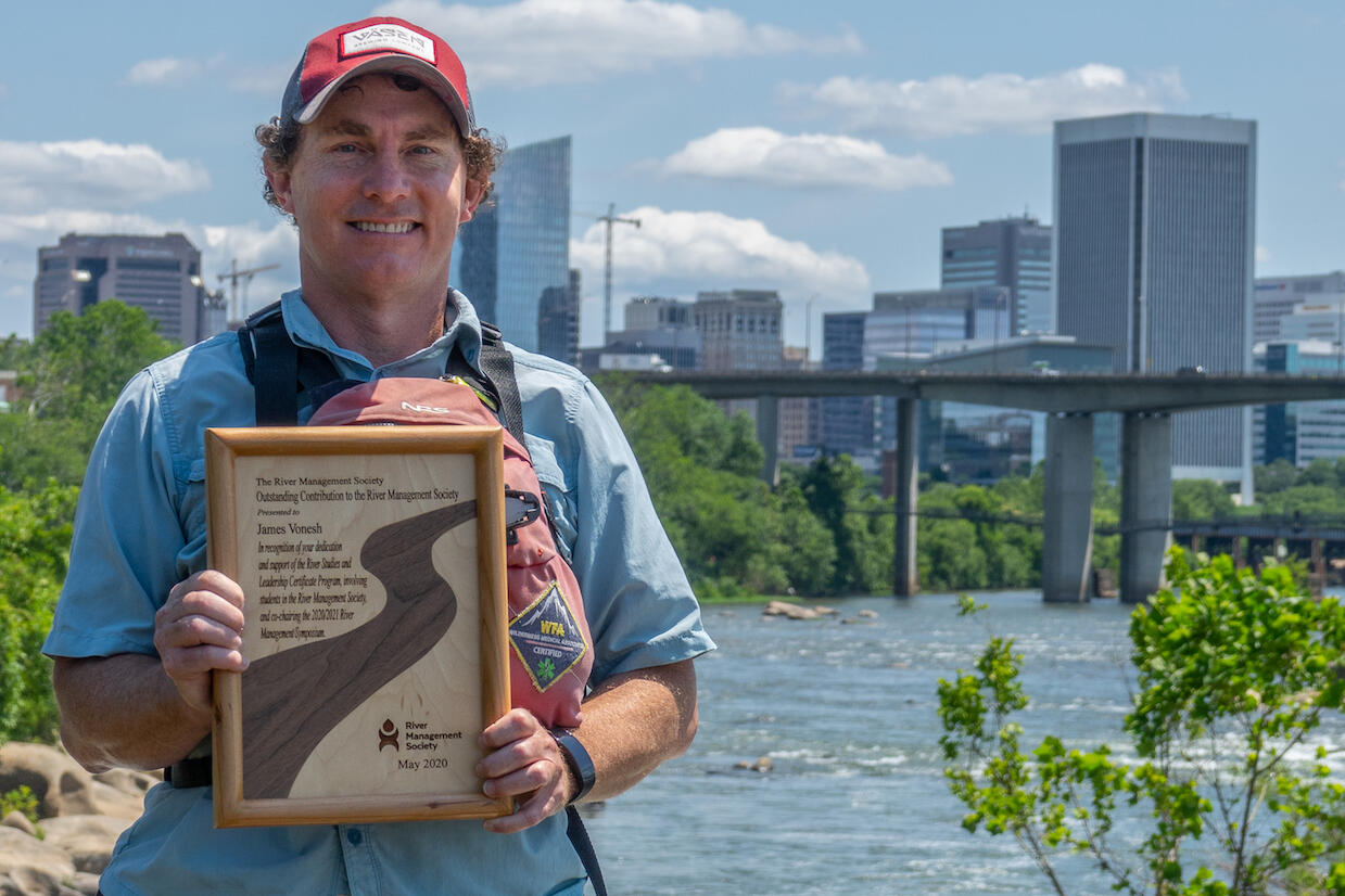 A person holding a plaque posed in front of the James River and Downtown Richmond.