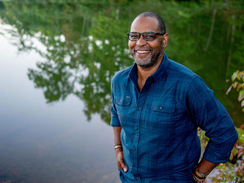 A photo of a man standing next to a lake while smiling. 